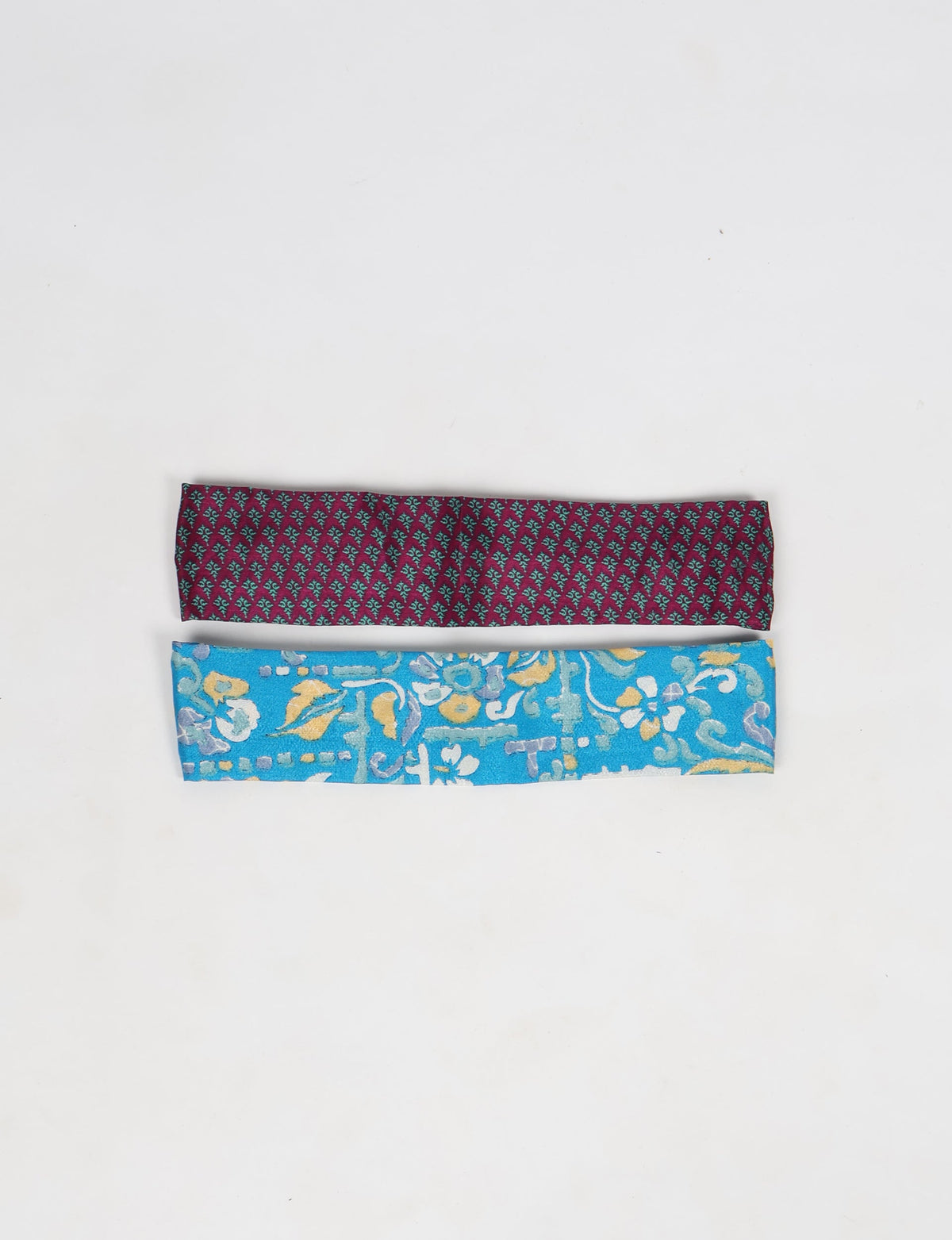 Set of two elastic headbands, one burgundy with small teal pattern, one blue with multicolor floral design, flat lay