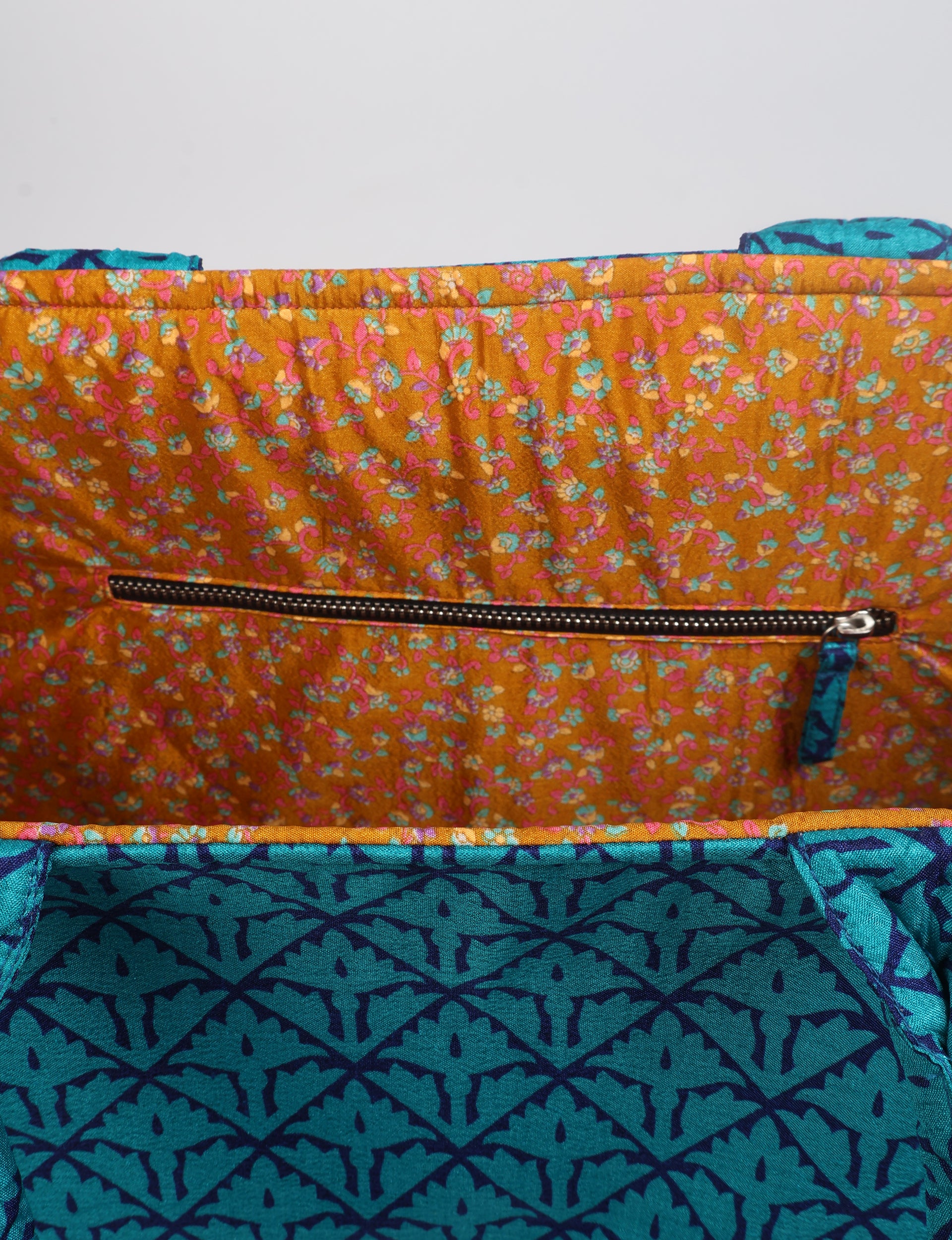 Interior view of a blue tropical patterned work tote bag with an orange floral zippered pocket and fabric pull tab