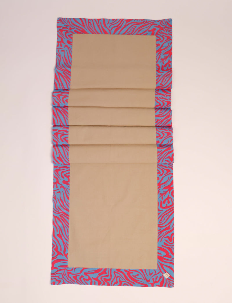 Beige table runner with blue and red abstract patterned border, shown flat with a small fabric tag on corner