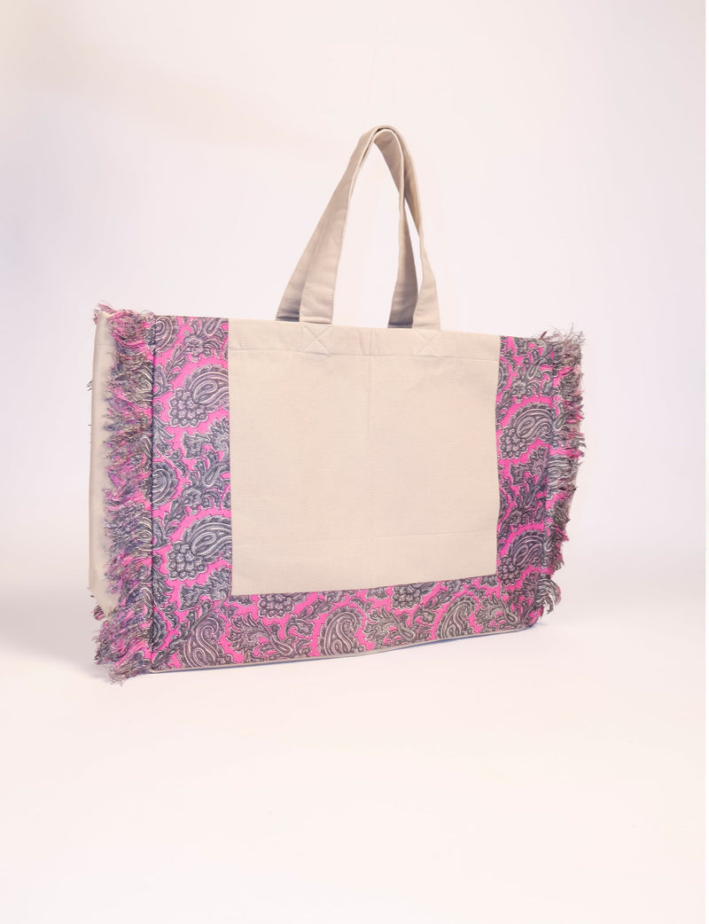 Beige carry-all bag with pink paisley patterned fabric and fringed edges, shown from front view on white background