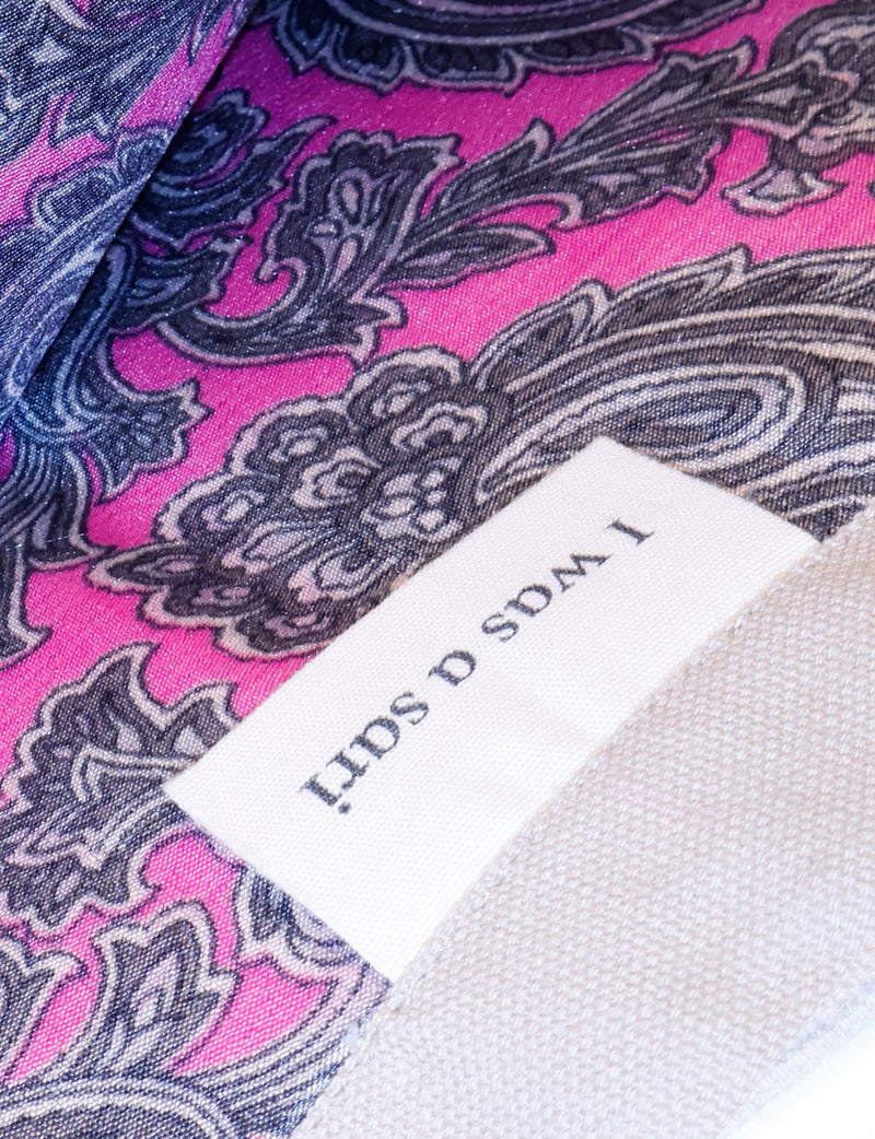 Close-up of pink paisley fabric with black and gray intricate patterns and a white label reading "TWODS SPITI"
