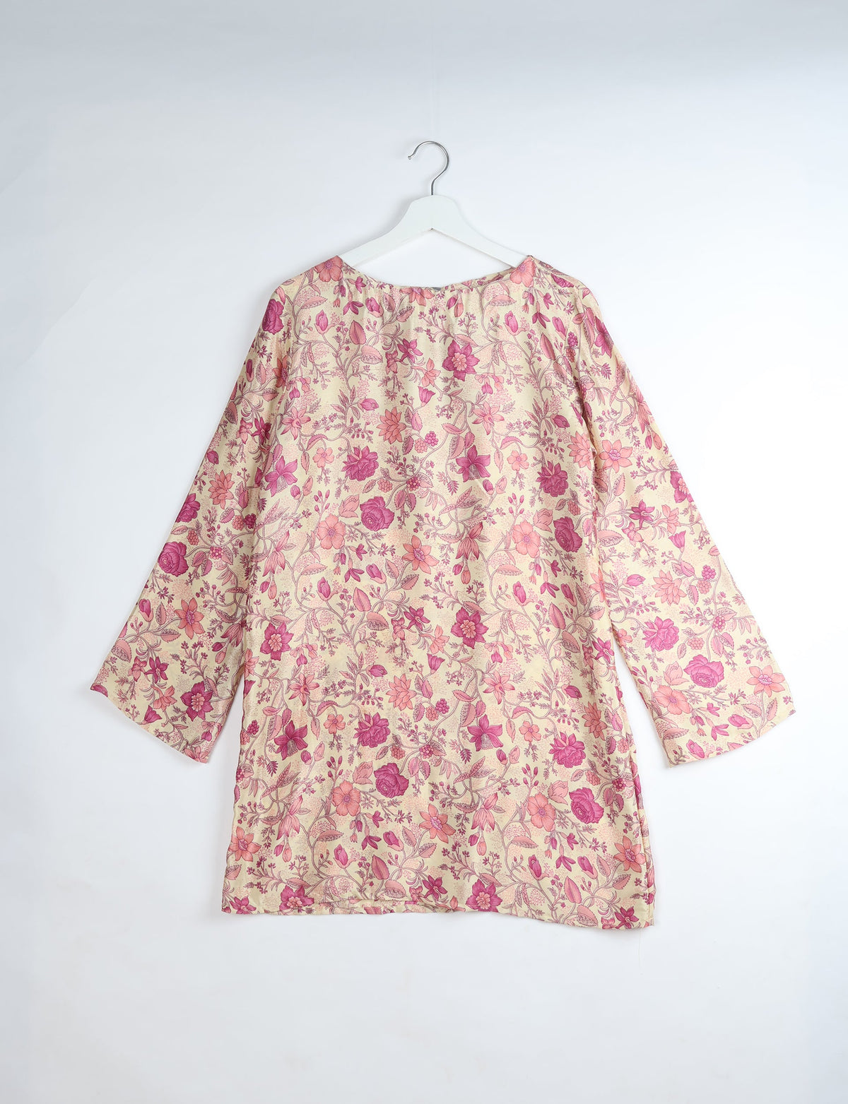 Long-sleeve swing dress with pink and purple floral print on beige fabric, shown hanging on white hanger, back view