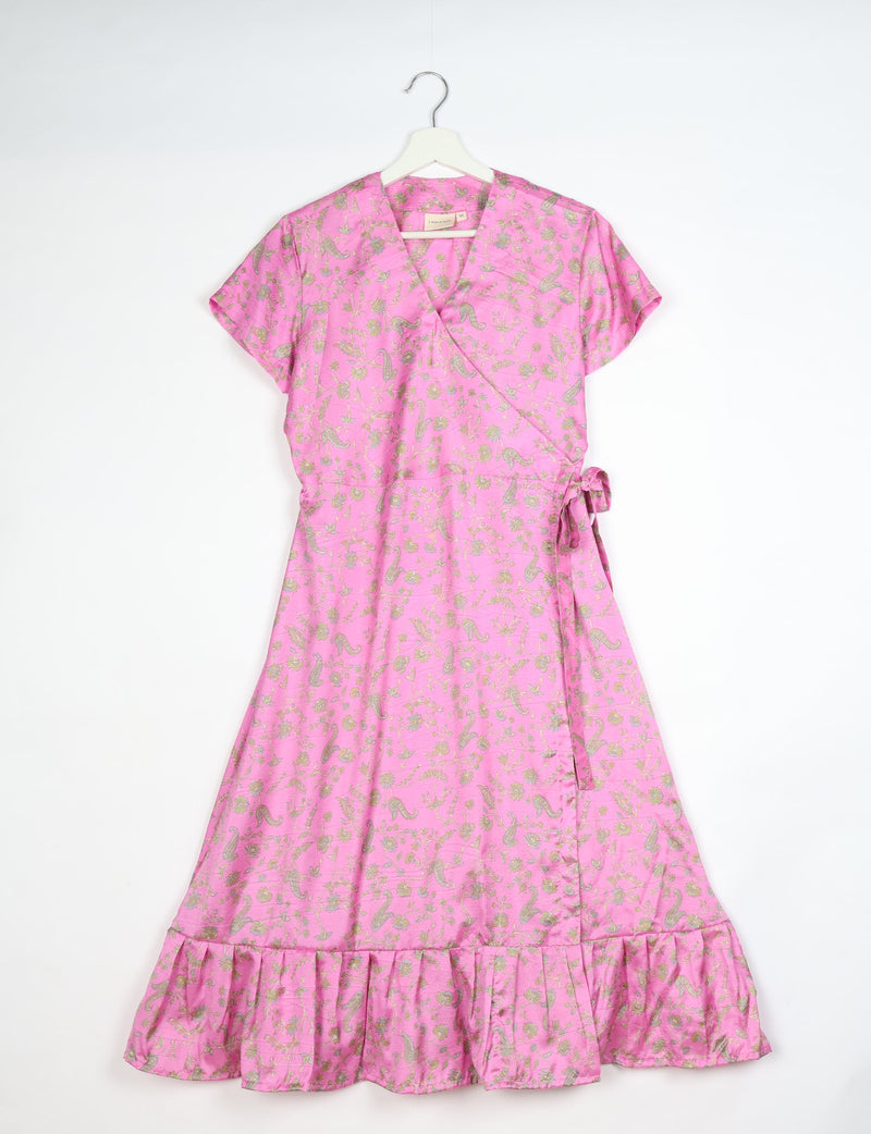 Pink midi wrap dress with tropical floral and paisley print, short sleeves, side tie, and ruffled hem, hanging on white