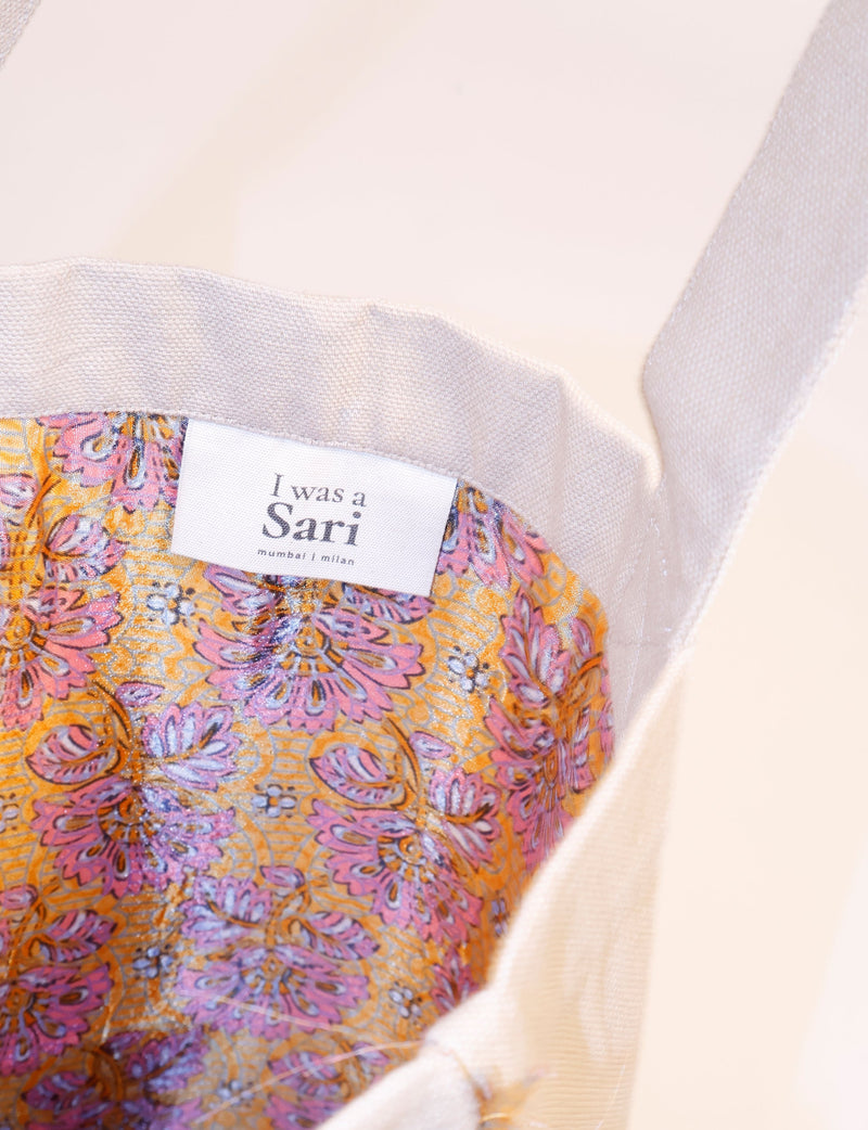 Yellow floral fabric interior of a fringe shopper bag with beige canvas strap and label reading "I was a Sari."