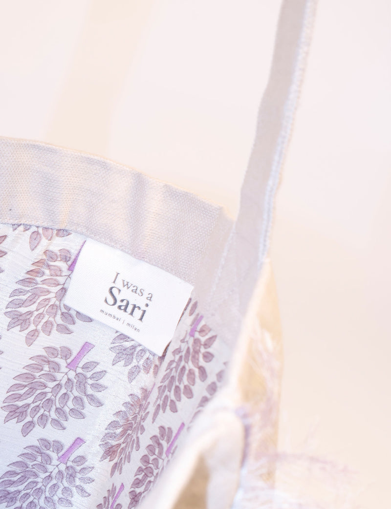 White fabric shopper bag with purple leaf pattern and label reading "I was a Sari mumbai | milan" inside the bag near the top edge