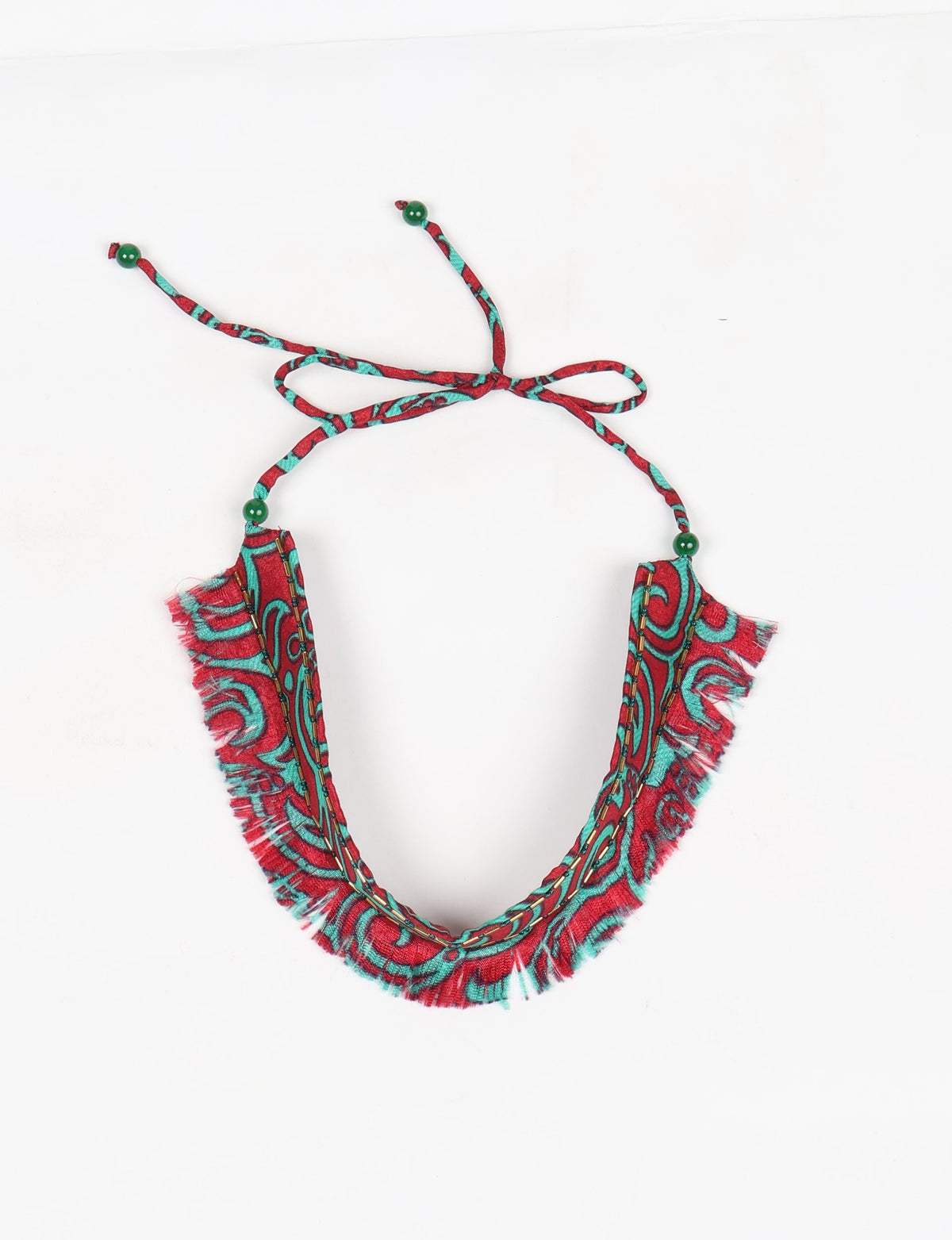 Red and turquoise abstract patterned fabric choker with fringe edges and green bead tie-up closure, flat lay view