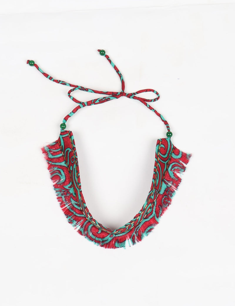 Red and turquoise abstract patterned fabric choker with fringe edges and green bead tie-up closure, flat lay view
