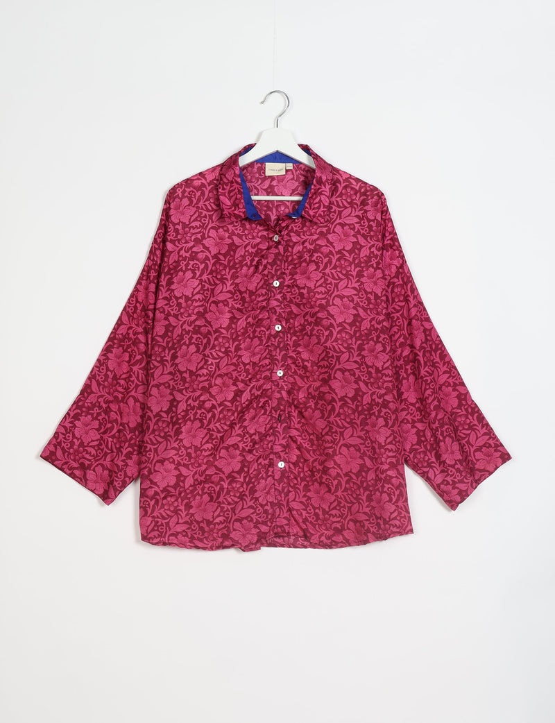 Pink oversized button-up shirt with floral pattern and blue inner collar, hanging on white hanger against white background