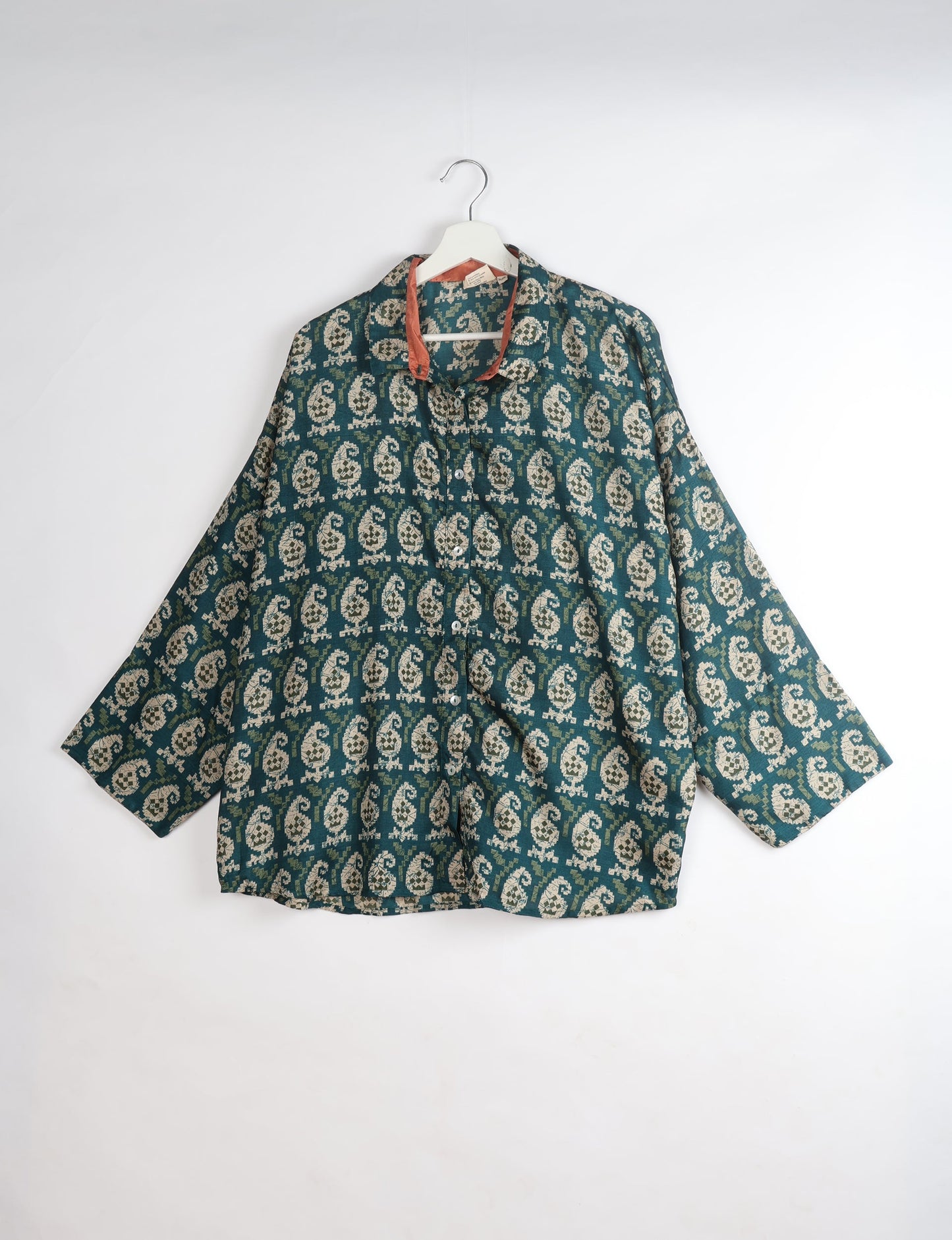Green oversized shirt with beige paisley pattern, button front, and contrasting rust-colored inner collar, hanging on white