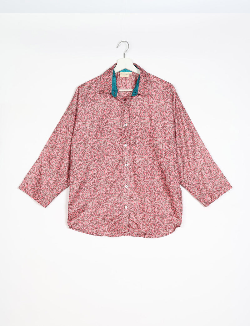 Pink oversized button-up shirt with floral swirl pattern and contrasting teal inner collar, hanging on white hanger