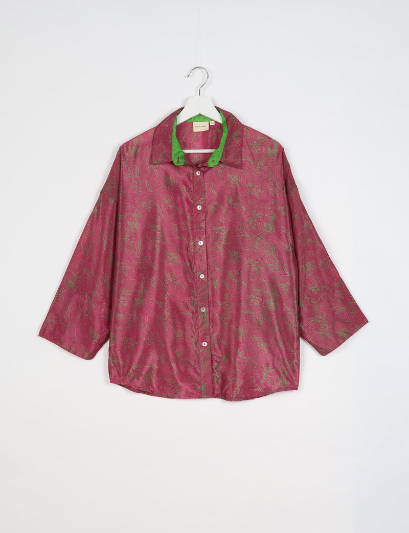 Pink oversized button-up shirt with green collar lining and subtle floral pattern, hanging on white hanger