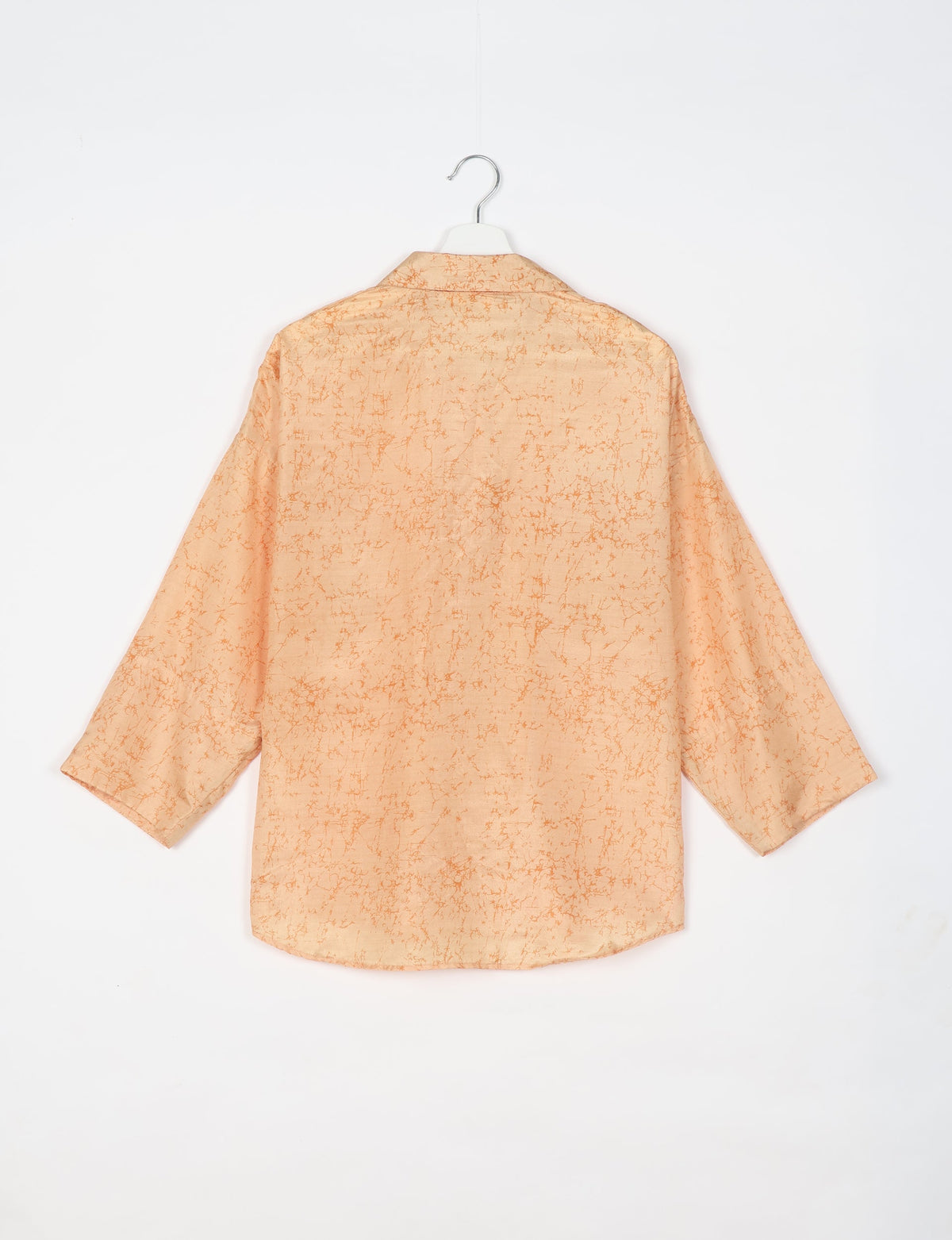 Oversized long-sleeve shirt in light orange with darker orange abstract pattern, shown from back on white hanger