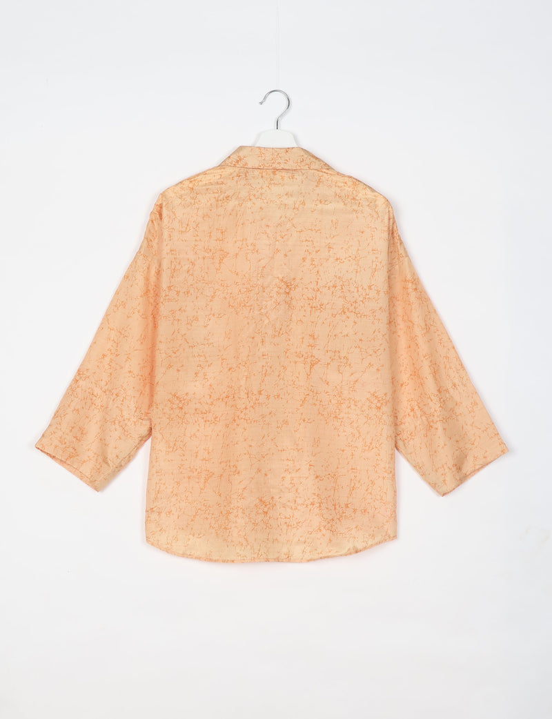 Oversized long-sleeve shirt in light orange with darker orange abstract pattern, shown from back on white hanger