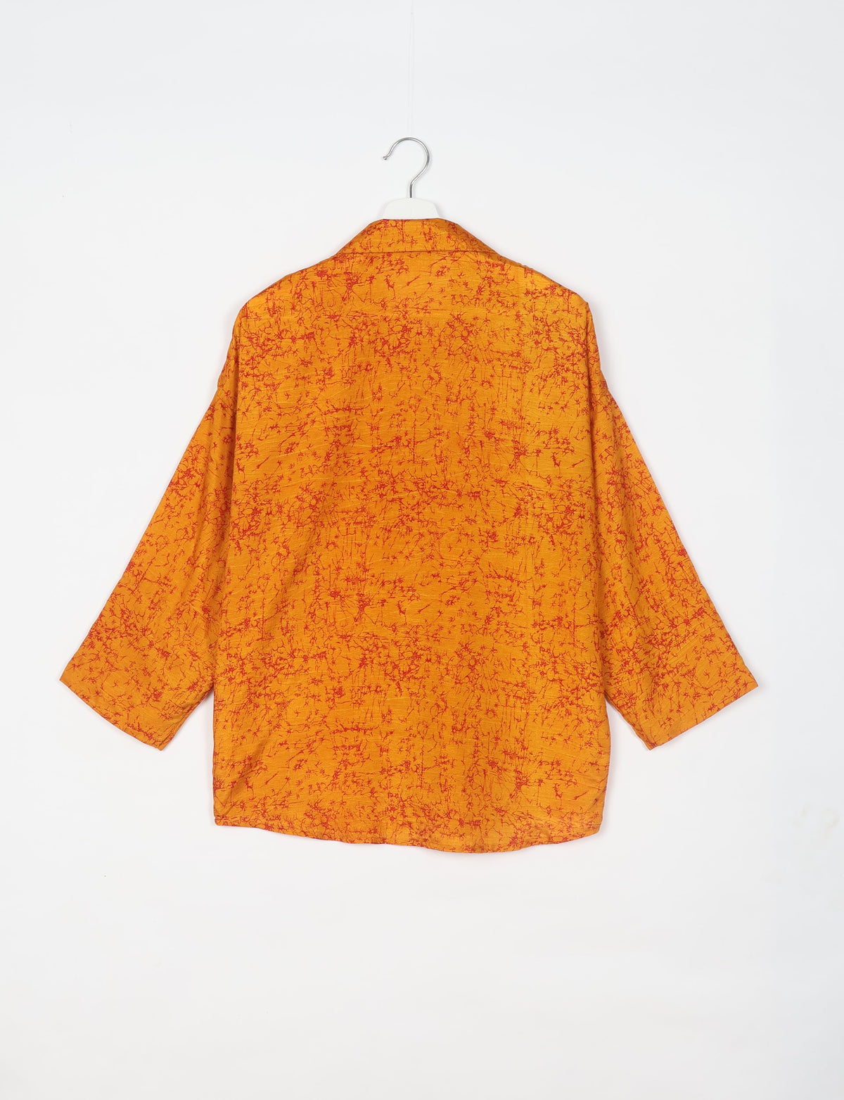 Oversized orange shirt with red abstract pattern, shown from the back, hanging on a white hanger against a white background