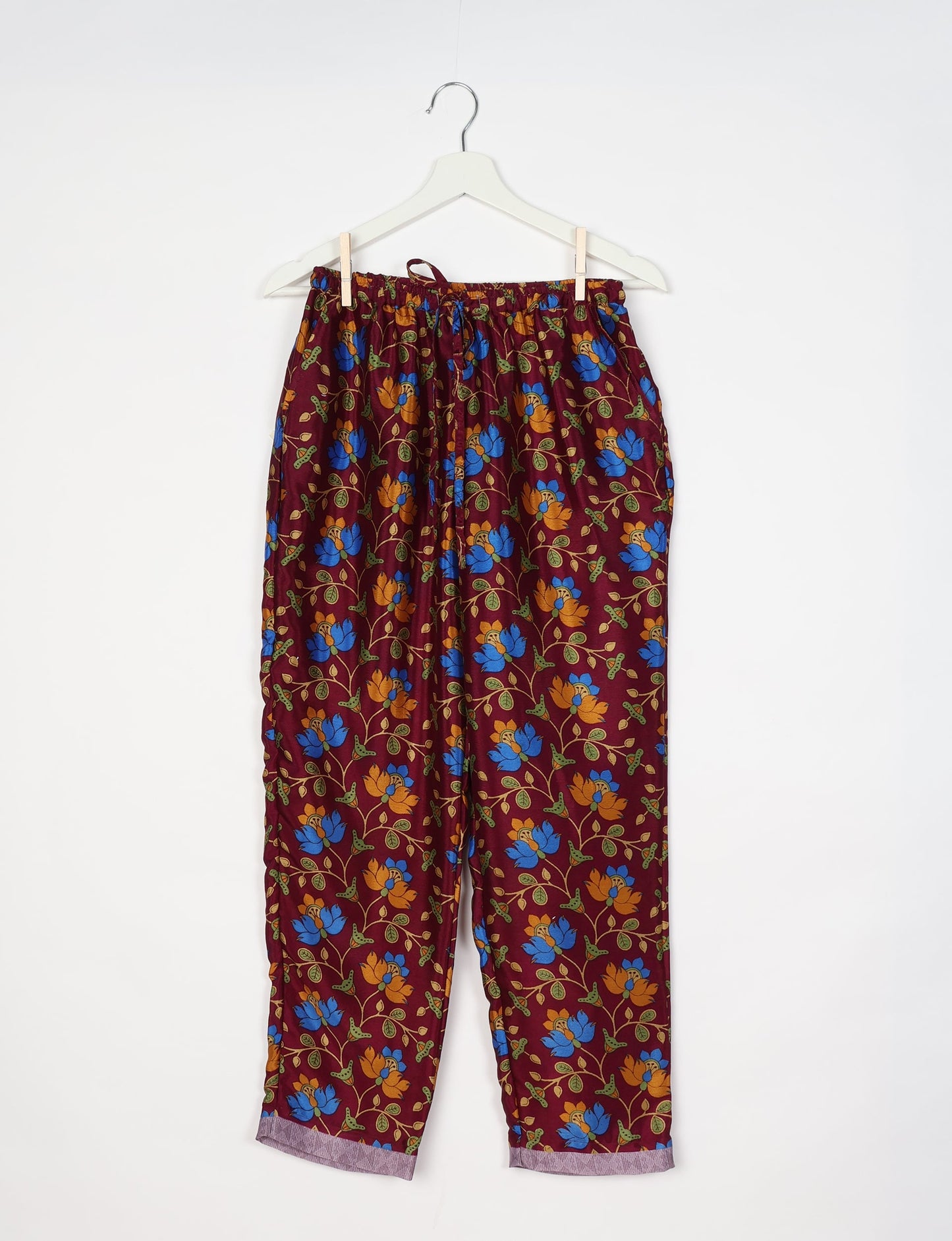 Red pull-on pants with blue and orange floral tropical print, elastic waistband with drawstring, hanging on white hanger