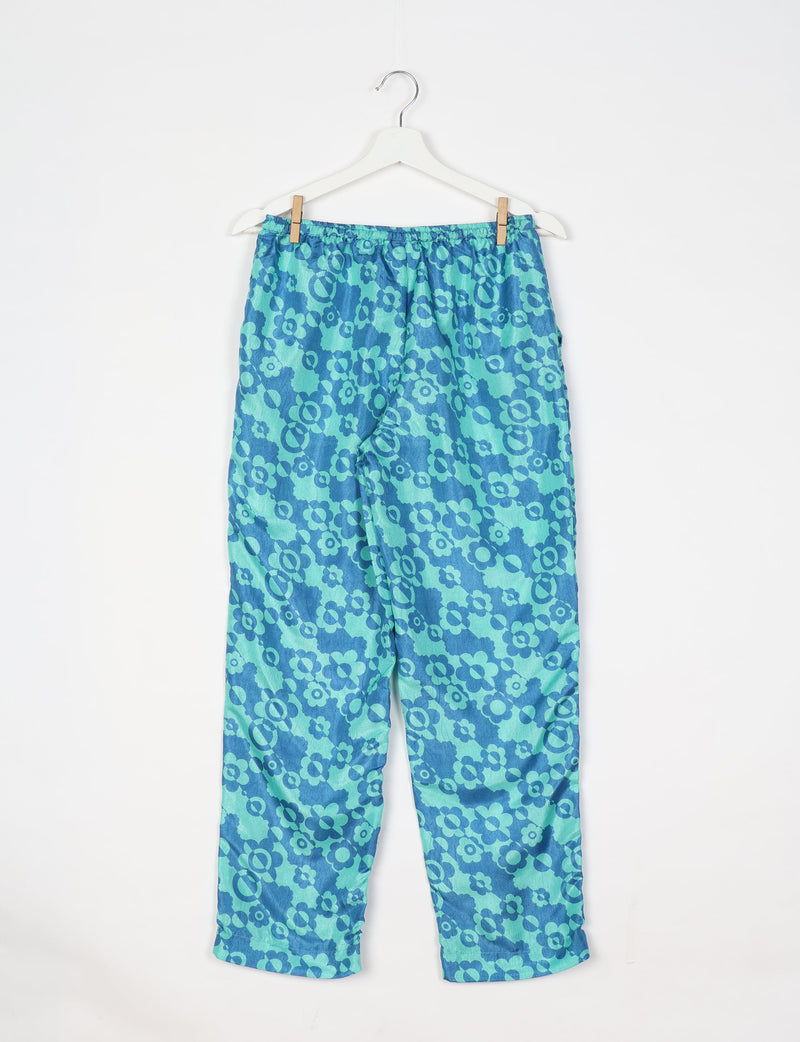 Blue pull-on pants with elastic waistband and all-over floral pattern hanging on white hanger against white background