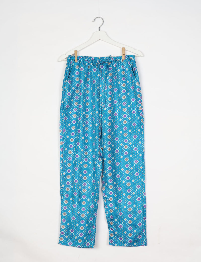 Blue pull-on pants with purple, white, and gray ikat pattern, elastic waistband with drawstring, hanging on white hanger