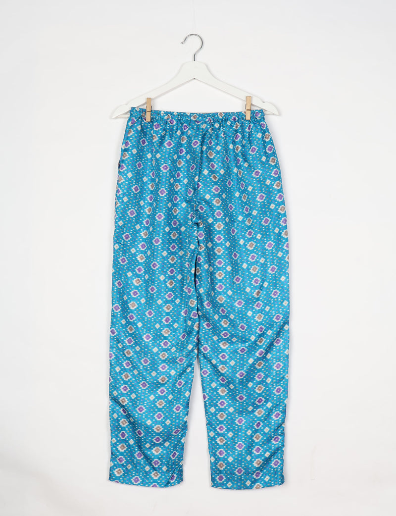 Blue pull-on pants with elastic waistband and purple, white, and gray ikat pattern hanging on white hanger
