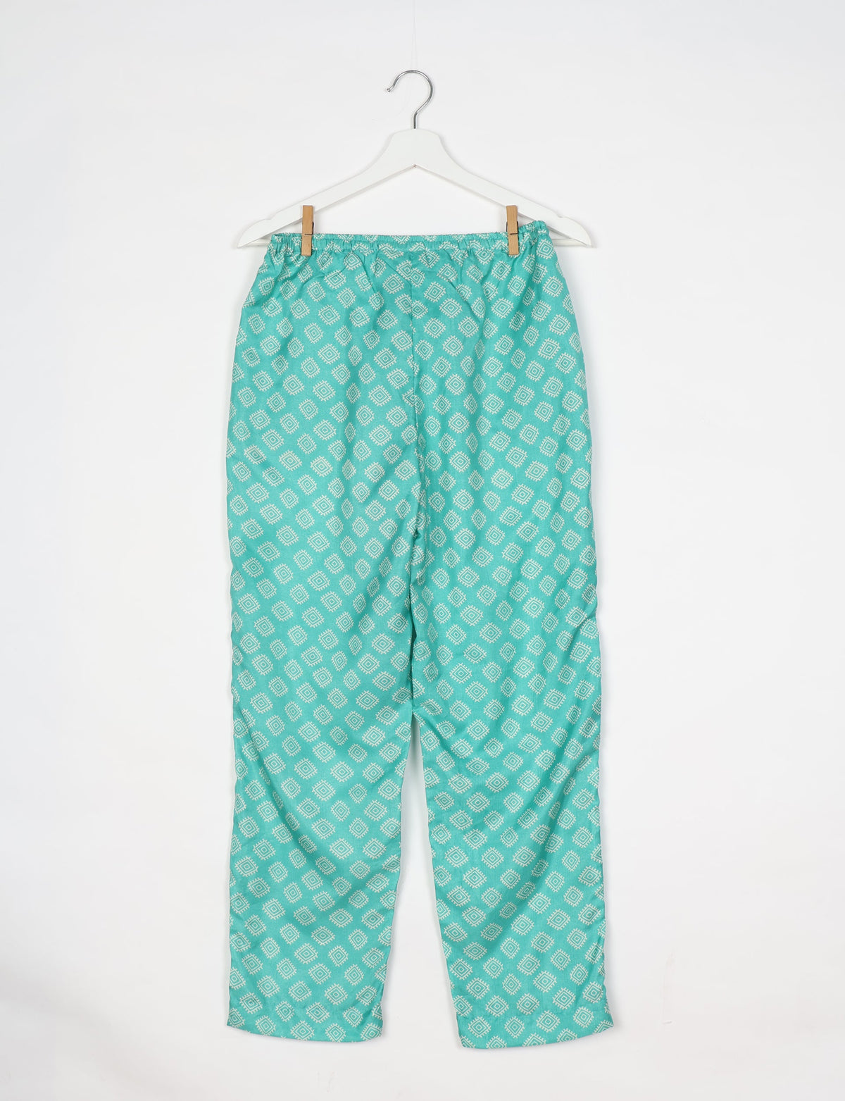 Green pull-on pants with white geometric diamond pattern hanging on white hanger against white background