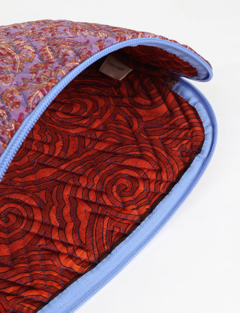 Quilted laptop sleeve with purple paisley exterior, red patterned interior, and light blue zipper, partially open showing label