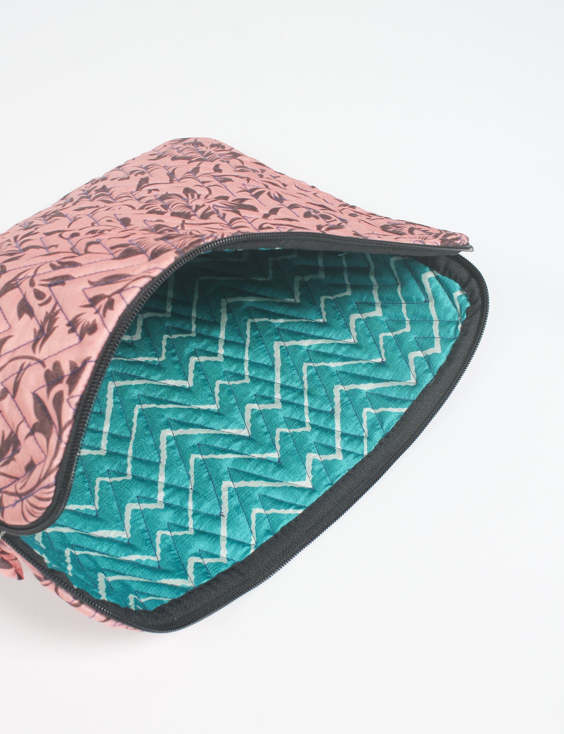 Quilted laptop sleeve with pink floral exterior and teal zigzag patterned interior, partially unzipped, flat lay