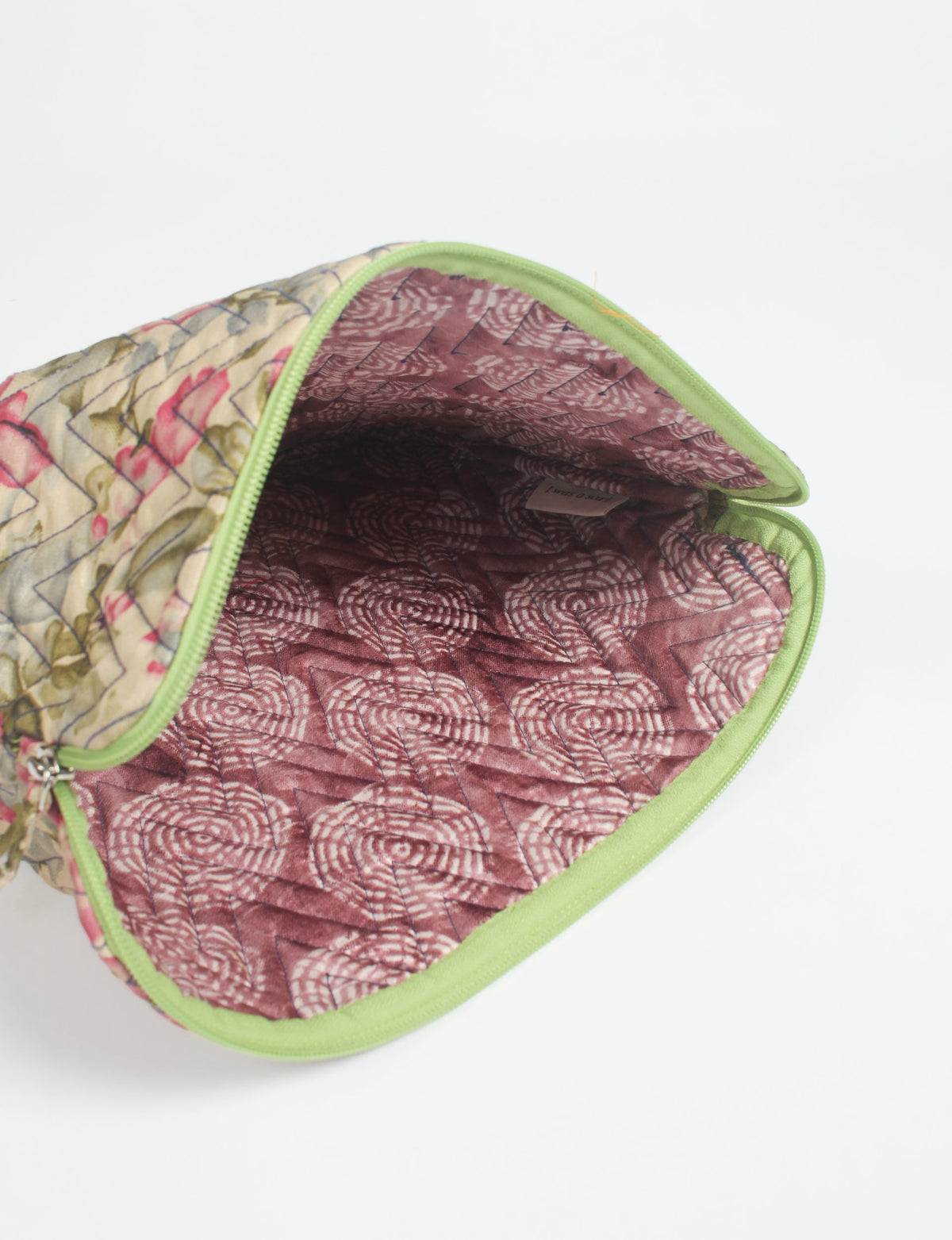 Quilted laptop sleeve with beige floral exterior, green zipper, and maroon patterned interior, shown open from top angle