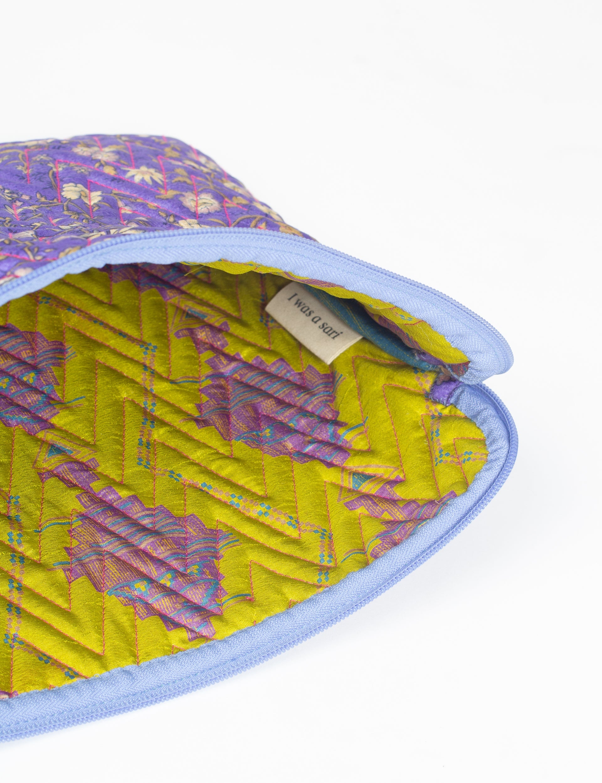 Quilted laptop sleeve with purple floral exterior, blue zipper, and yellow patterned interior showing "I was a sari" label