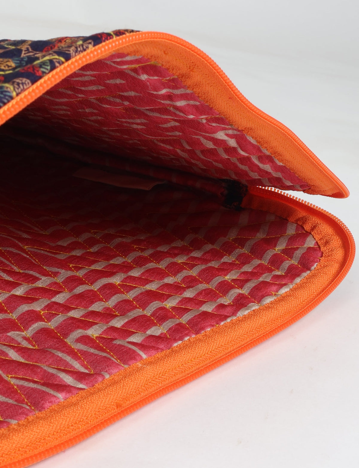 Quilted laptop sleeve with orange trim, red patterned interior, and blue tropical patterned exterior, shown open from inside view
