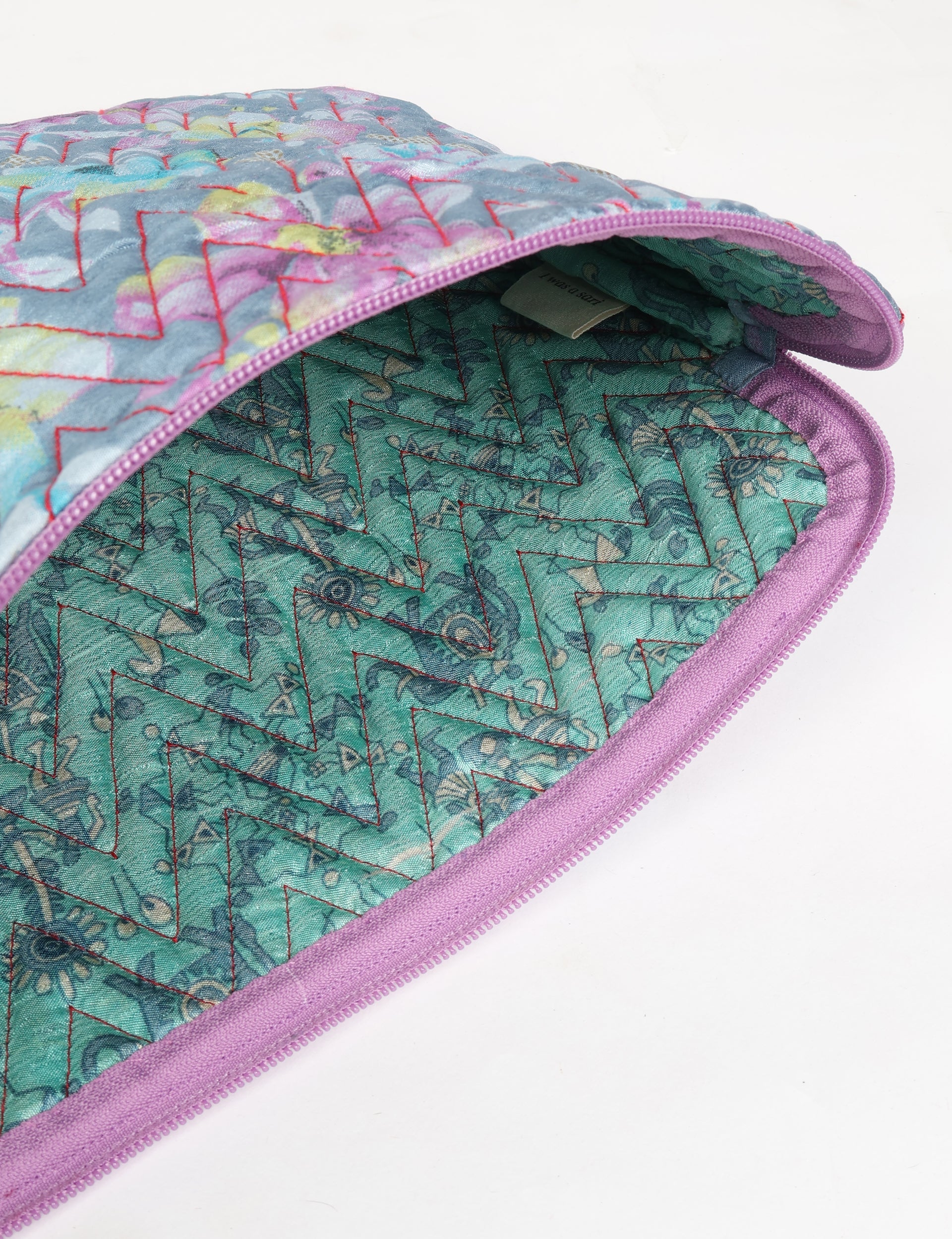 Quilted laptop sleeve with grey floral exterior, purple zipper, and teal patterned interior, shown partially open