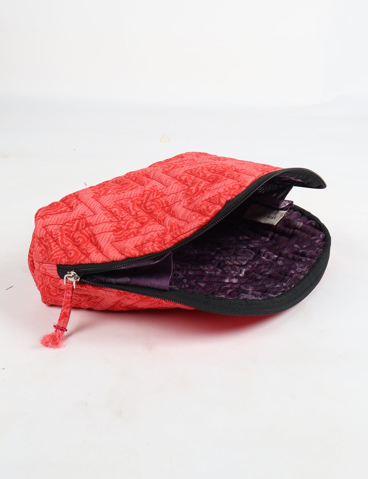 Pink tropical patterned quilted vanity pouch with black zipper and purple textured interior, partially open on white background