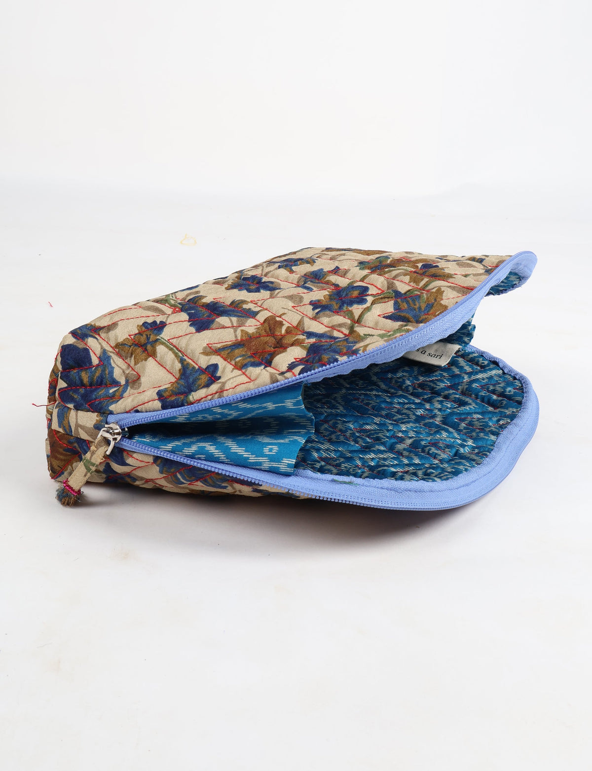 Beige quilted vanity pouch with blue and brown leaf pattern, blue zipper, and blue patterned fabric interior, partially open