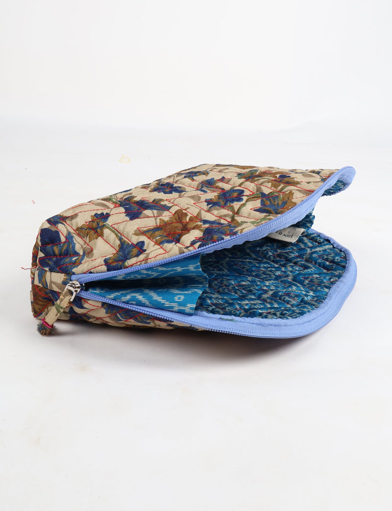 Beige quilted vanity pouch with blue and brown leaf pattern, blue zipper, and blue patterned fabric interior, partially open