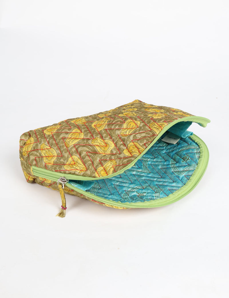 Quilted vanity pouch with yellow tropical leaf pattern exterior and blue patterned interior, green zipper partially open