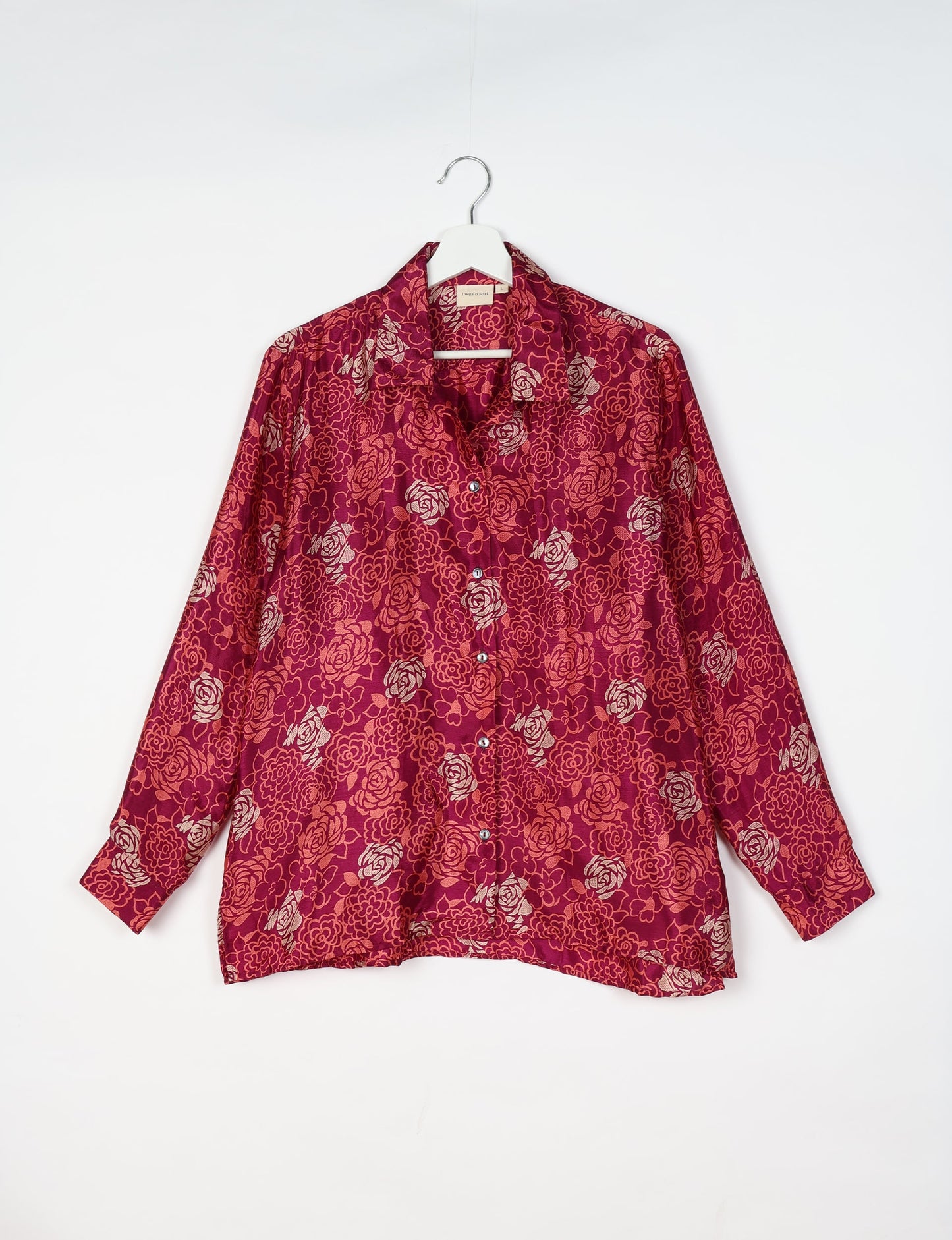 Long-sleeve pink floral resort shirt with button front and collar, hanging on white hanger against white background