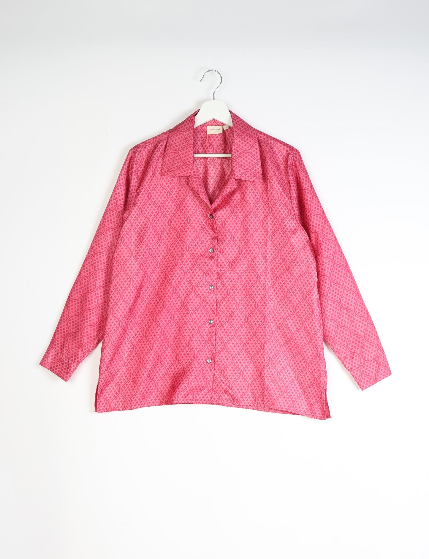 Red tropical patterned long-sleeve resort shirt with collar and buttons, hanging on white hanger against white background