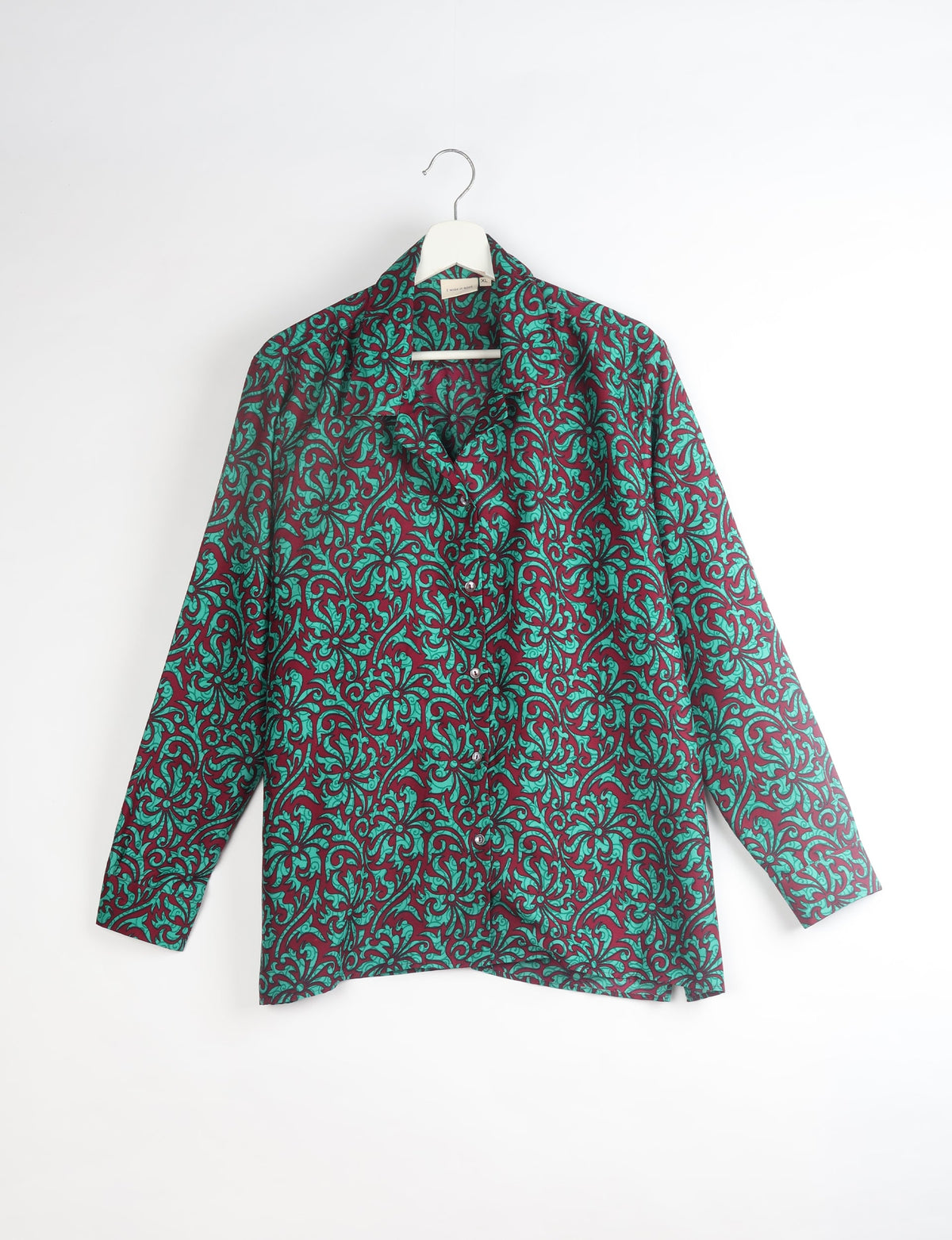 Long-sleeve button-up resort shirt with teal leaf pattern on red background, hanging on white hanger, front view