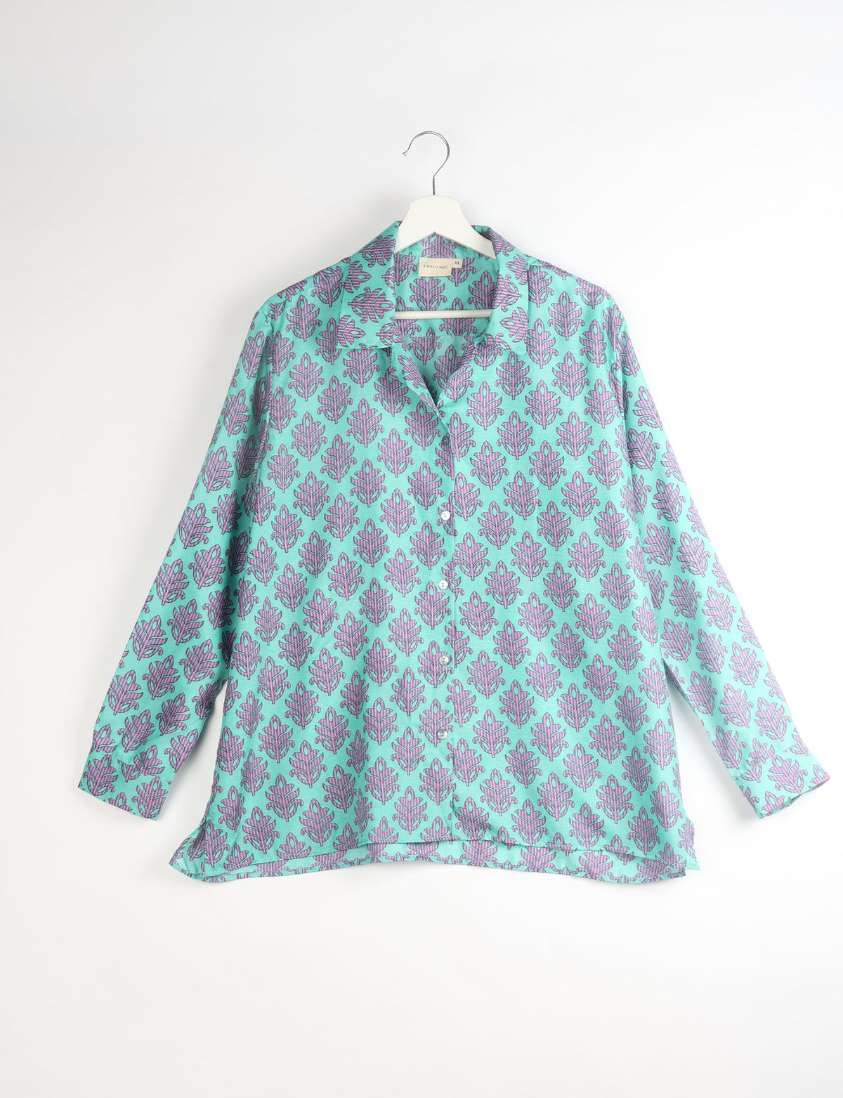 Long-sleeve button-up resort shirt with purple leaf pattern on turquoise background, shown hanging on white hanger