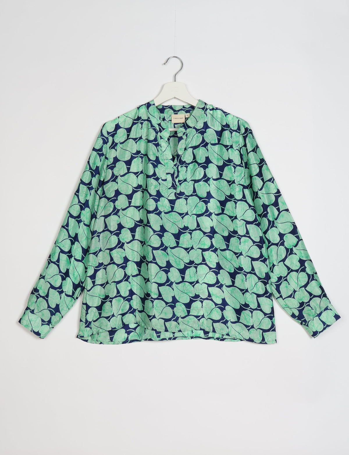 Long-sleeve blouse with blue background and green leaf pattern, V-neckline, hanging on white hanger against white background