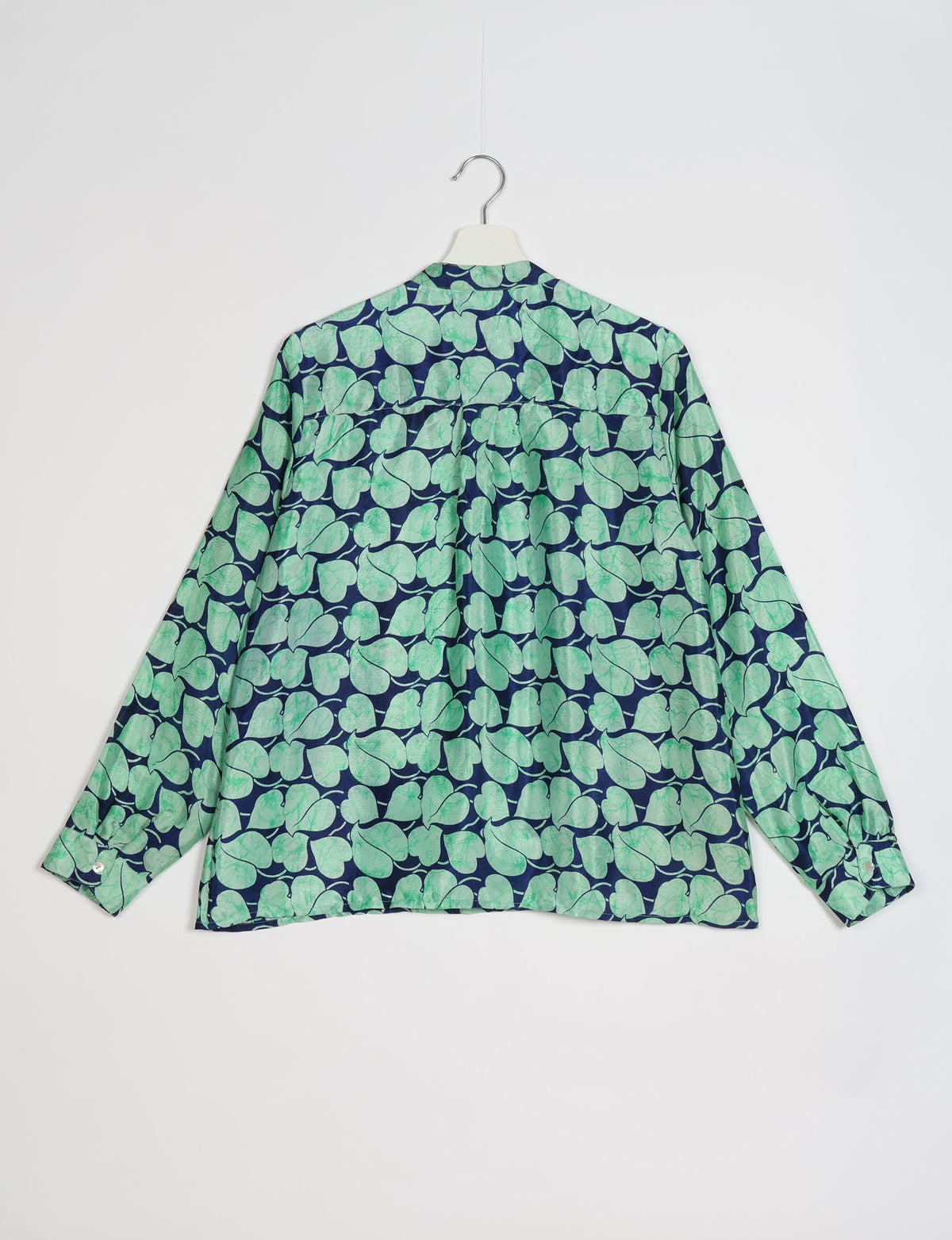 Long-sleeve blouse with blue background and green leaf pattern, shown from back on white hanger against white background