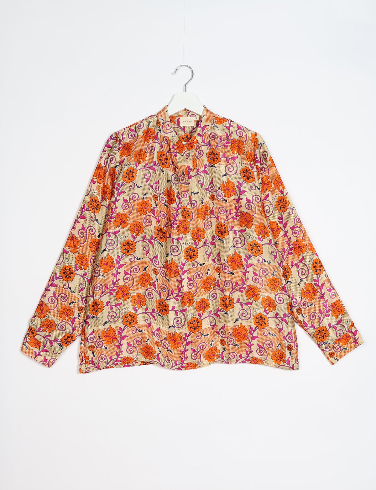 Orange floral patterned blouse with long sleeves and a collar, hanging on a white hanger against a white background