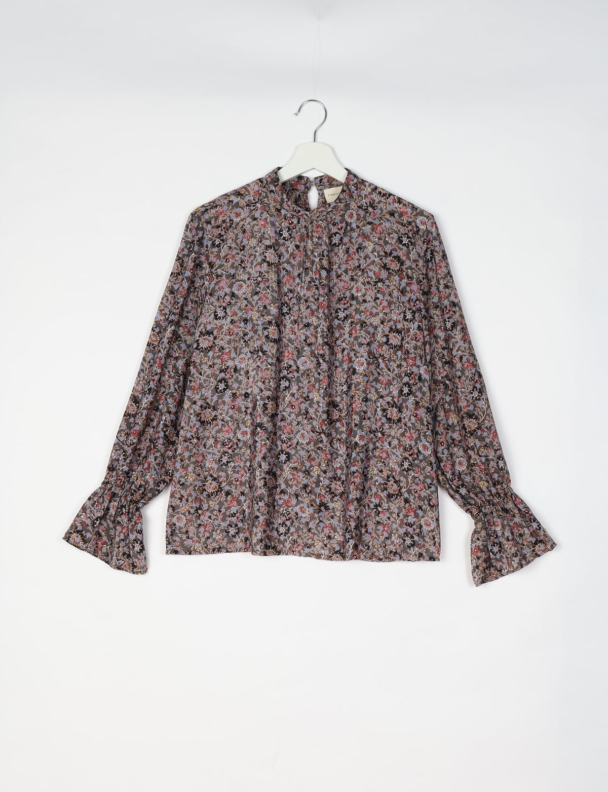 Black blouse with multicolor floral print, long sleeves with ruffled cuffs, and a keyhole neckline, hanging on white hanger