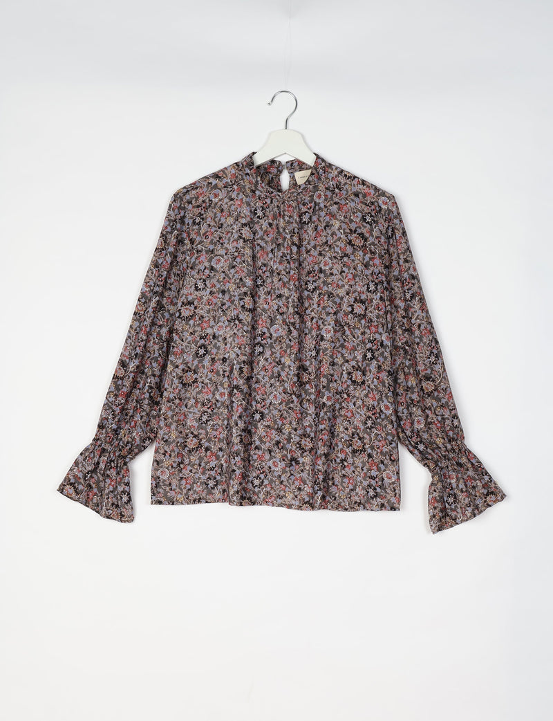 Black blouse with multicolor floral print, long sleeves with ruffled cuffs, and a keyhole neckline, hanging on white hanger