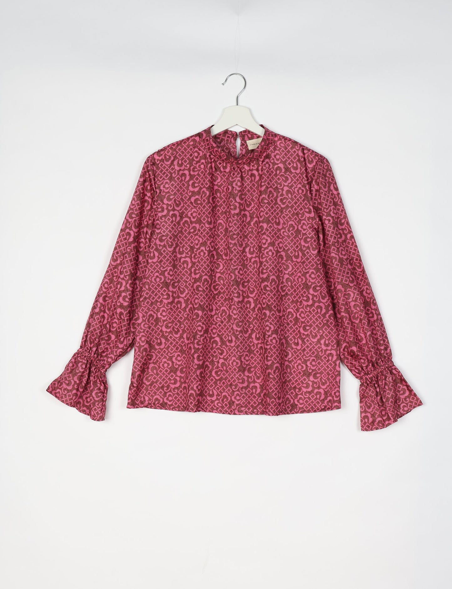 Pink blouse with dark pink geometric and floral pattern, long sleeves with gathered cuffs, and a keyhole neckline, hanging