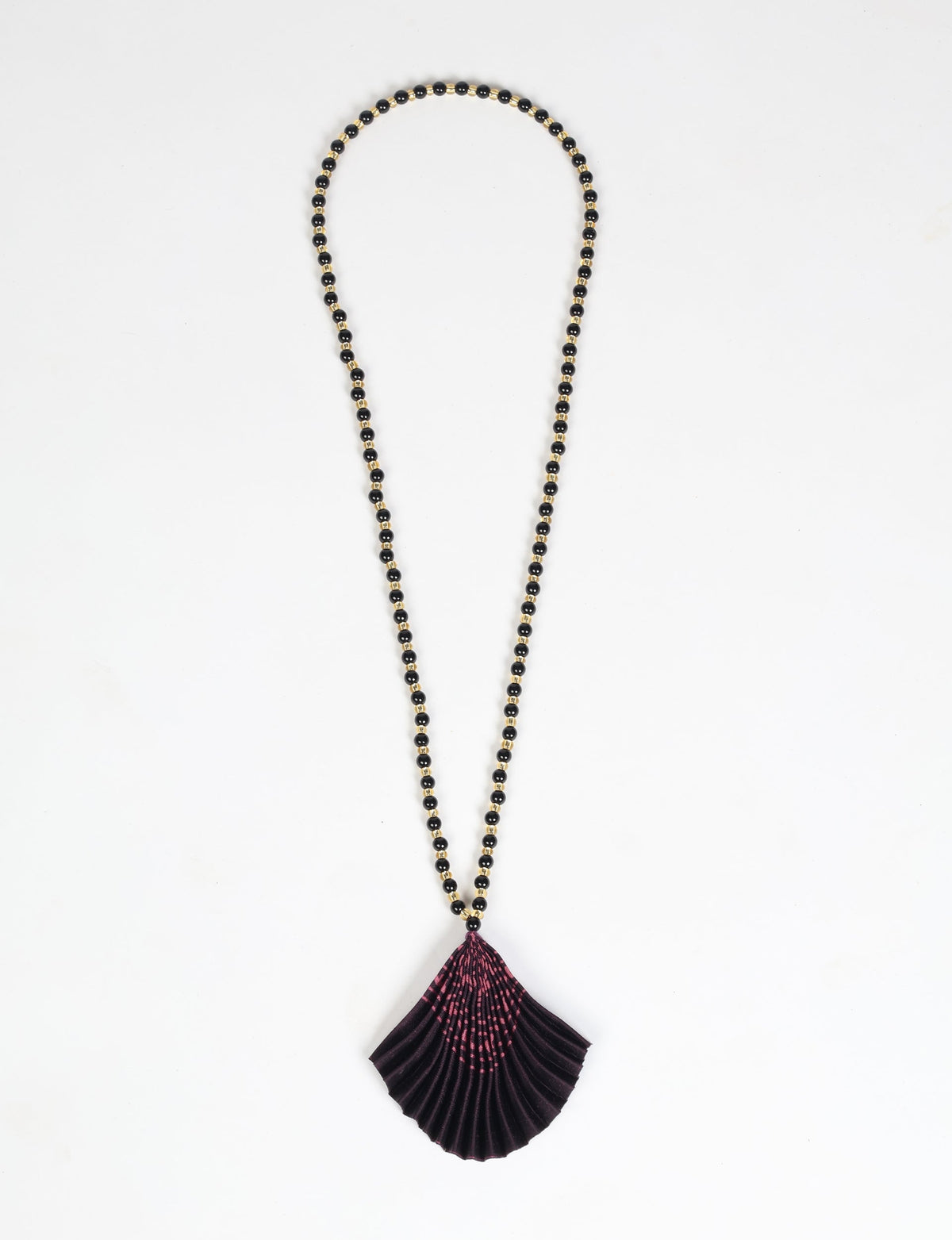 Necklace with black and gold beads and a pleated dark purple fabric pendant with pink abstract pattern, flat lay