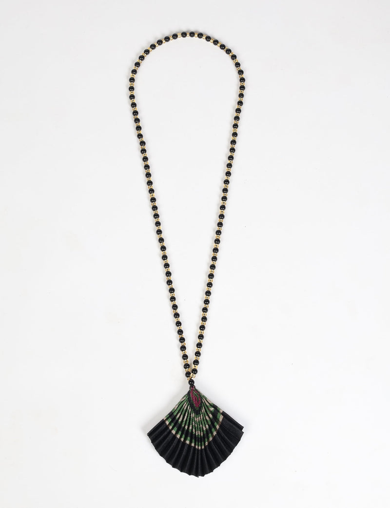 Necklace with black and gold beads and a pleated fan-shaped pendant in black, green, and purple, flat lay on white background