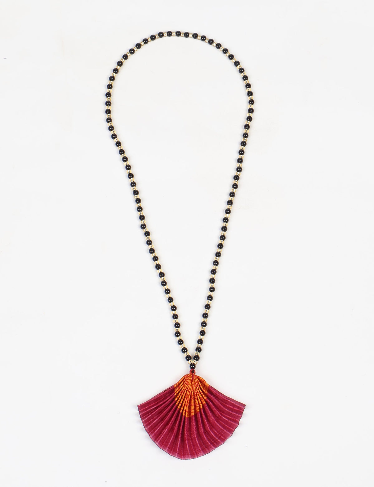 Necklace with black and gold beads and a pleated pink and orange abstract fan-shaped pendant, flat lay on white background