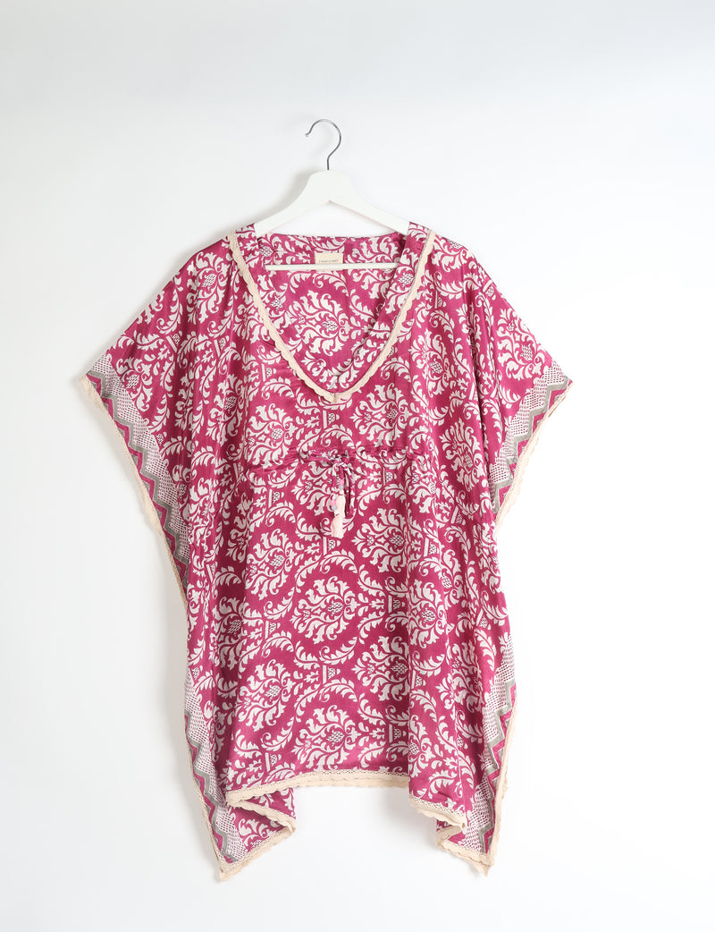 Pink tropical short kaftan with white floral pattern, lace trim, V-neck, and drawstring waist, hanging on white hanger