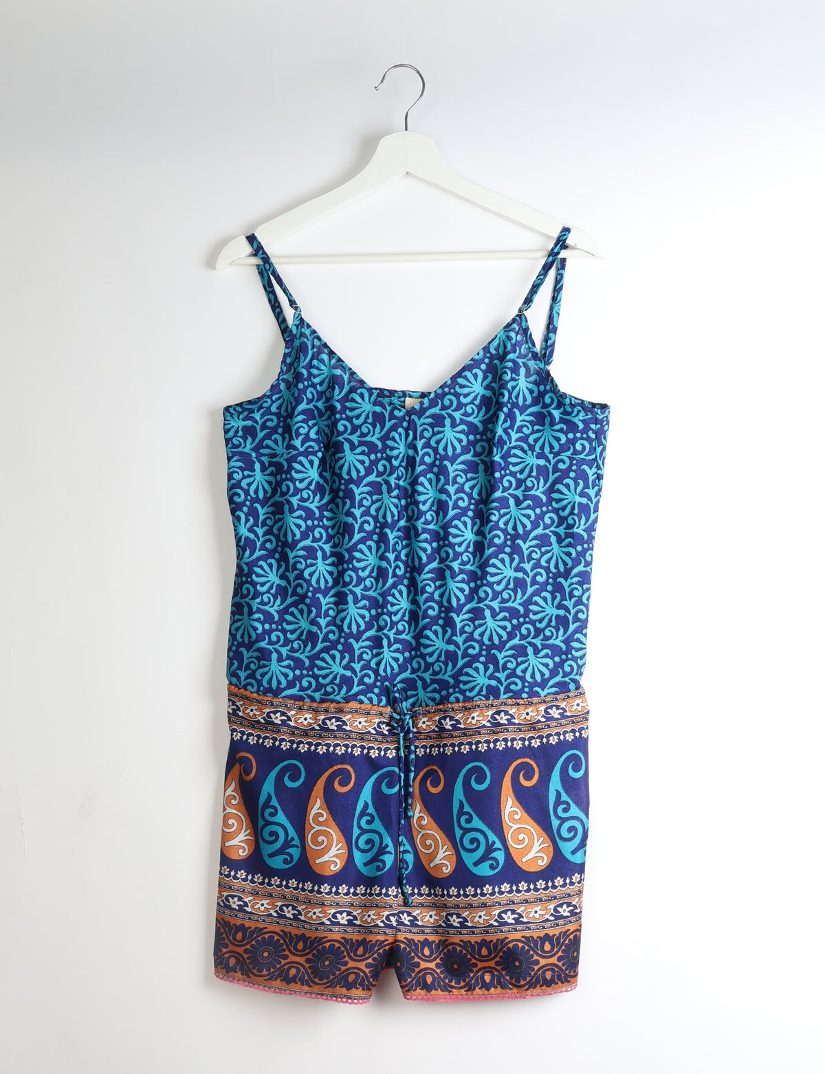 Blue playsuit with adjustable straps, lace trim, and blue and orange leaf and swirl patterns, hanging on white hanger