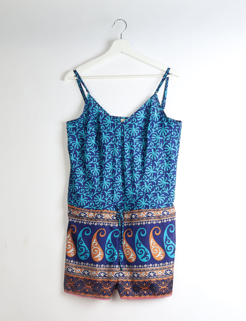 Blue playsuit with adjustable straps, lace trim, and blue and orange leaf and swirl patterns, hanging on white hanger
