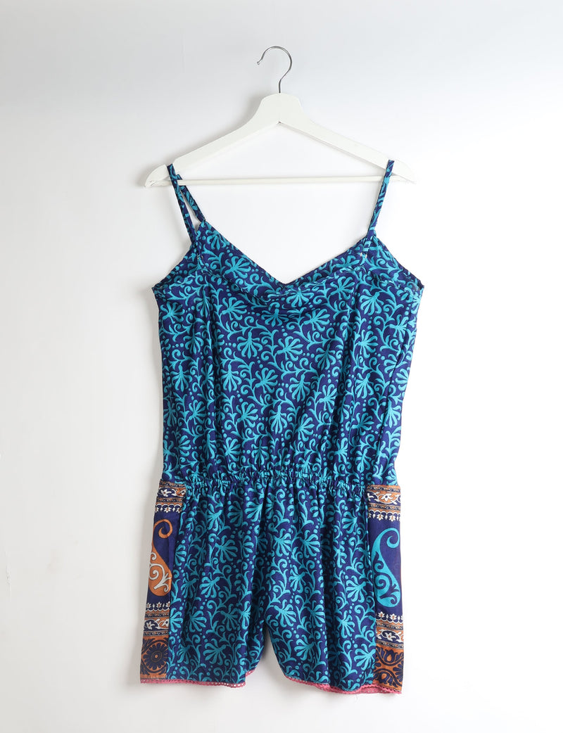 Blue playsuit with leaf pattern, adjustable straps, elastic waist, and lace trim on hem, hanging on white hanger